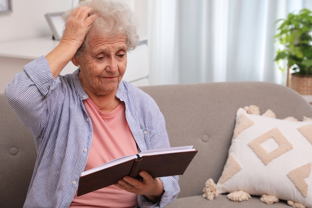 Senior woman with notebook at home, space for text. Age-related memory impairment