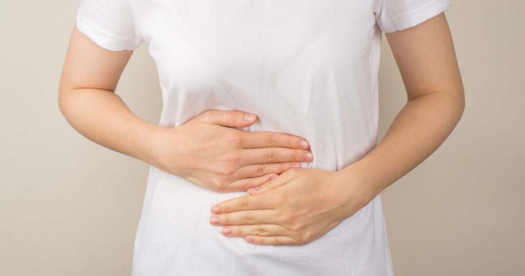 Cropped closeup photo of young woman in white t-shirt and jeans holding her hands on upper abdomen on isolated grey background