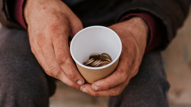 Front view of homeless man holding cup with coins