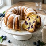 Sliced lemon blueberry pound cake with glaze dripping down the sides on a cake stand